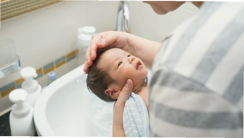 Bé sơ sinh đang nằm chơi trên thảm với đồ chơi xung quanh